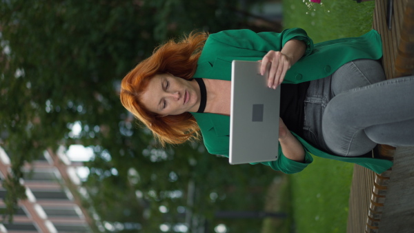 Young redhead woman sitting in a city park and using laptop.