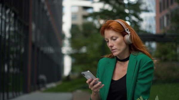 Young woman sitting in a city with smartphone and listening to music.