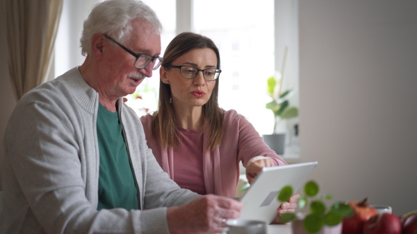 An adult daughter visiting her senior father at home and using tablet.