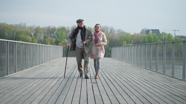 A senior man with daughter outdoors on a walk on pier by river.