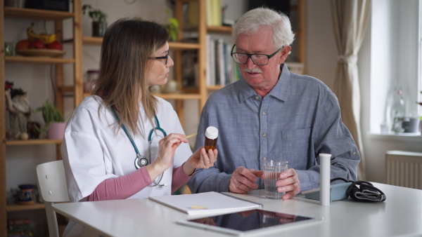 A healthcare worker or caregiver visiting senior man indoors at home, explaining medicine dosage.