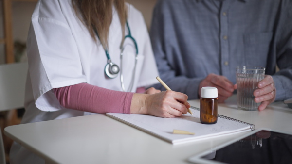 A healthcare worker or caregiver visiting senior man indoors at home, explaining medicine dosage.