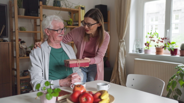 A happy woman surprising her senior father when visiting him at home and bringing present.