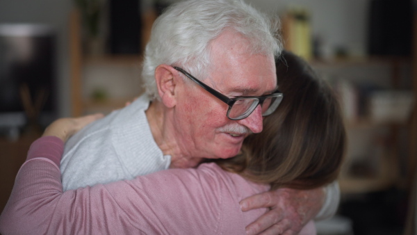 A rear view of adult daughter hugging her senior father when visitng him at home.