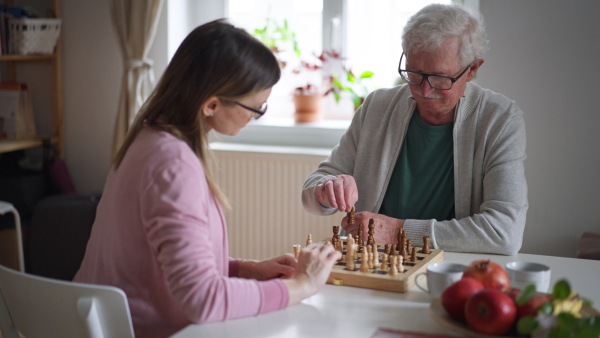 An adult daughter visiting her senior father at home and playing chess together.