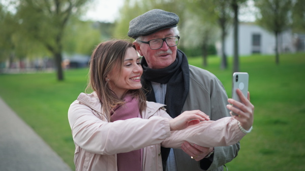 A happy senior man and his adult daughter taking selfie outdoors on a walk in park.