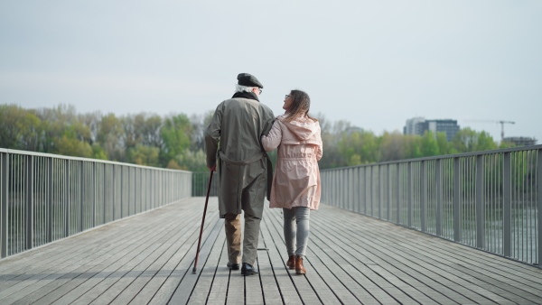 A rear view of senior man with daughter outdoors on a walk on pier by river.