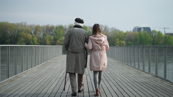 A rear view of senior man with daughter outdoors on a walk on pier by river.