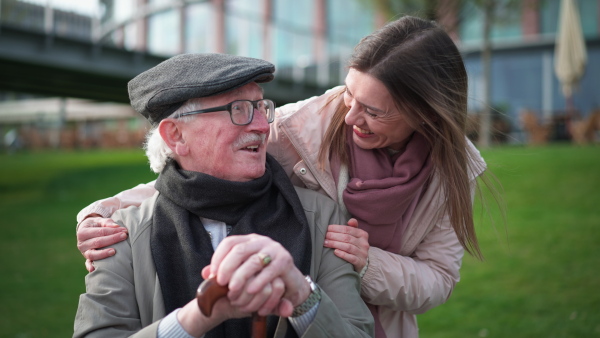 A happy senior man with his adult daughter sitting outdoors in park.