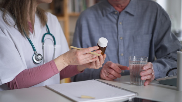 A healthcare worker or caregiver visiting senior man indoors at home, explaining medicine dosage.