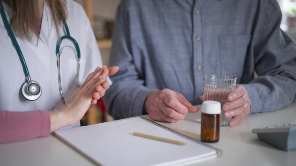 A healthcare worker or caregiver visiting senior man indoors at home, explaining medicine dosage.