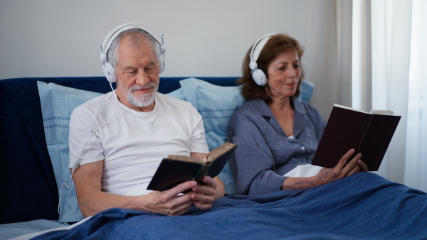 Happy senior couple listening music and reading books together in their bedroom.