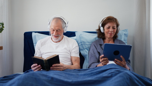 Senior couple in bed, reading book and digital tablet.