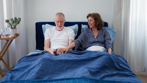 Senior couple sitting in bed and holding each other hand.