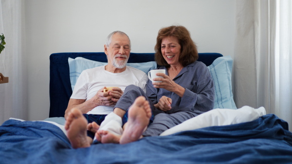 Happy senior couple enjoying cup of morning coffee together in their bed.