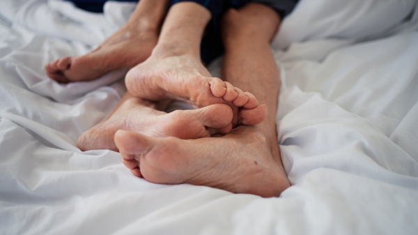 Close-up of feet touching. Senior couple in bed.