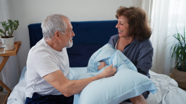 Happy senior couple in bed having fun, playing with pillow.