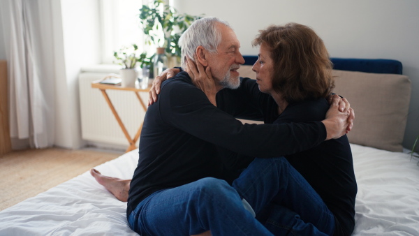 Happy senior couple in love sitting on a bed and huging.