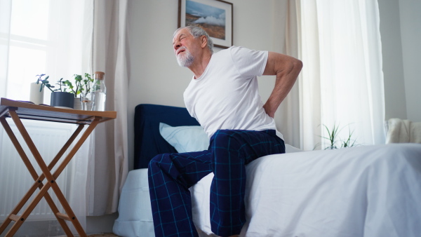 Senior man suffering from back pain after sleeping at home.