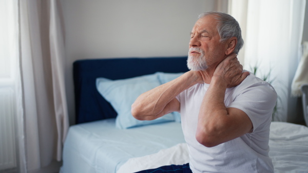 Senior man suffering neck pain in the morning on his bed.