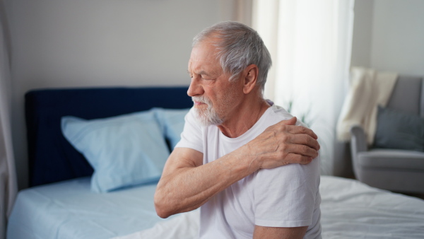 Senior man having pain in his shoulder, sitting in pyjama on bed.