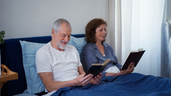 Happy senior couple reading books together in their bedroom.