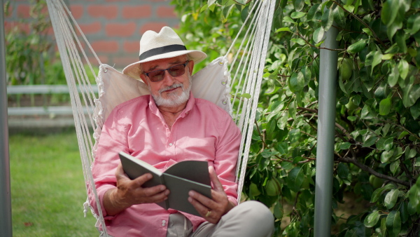 Elderly man resting in garden swing, reading a book.