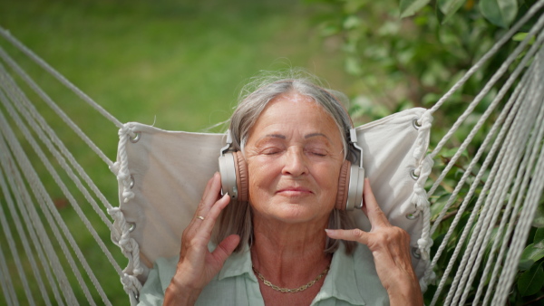 Mature elderly woman in garden swing listening to music with closed eyes.