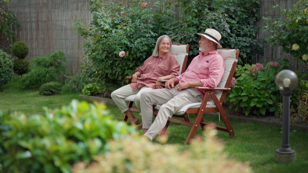 Elderly couple sitting in garden chairs, resting, talking to each other. .