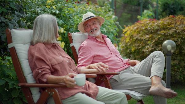 Elderly couple sitting in garden, relaxing, talking. Enjoying to age together.