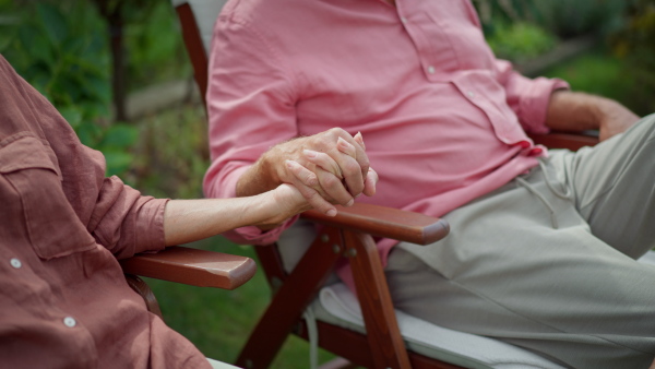 Close up of elderly couple holding hands sitting in garden chairs. Happy together.