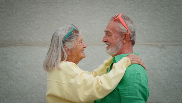 Colourful portrait of loving happy senior couple touching each ither with noses, with white wall in background.