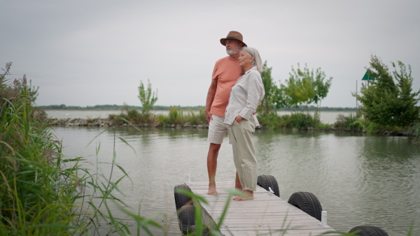 Elderly couple enjoying time at riverside, standing on wooden pier.