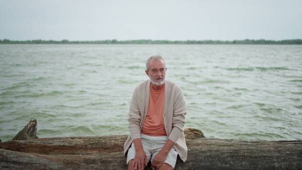 Senior man sitting on drift wood on beach.