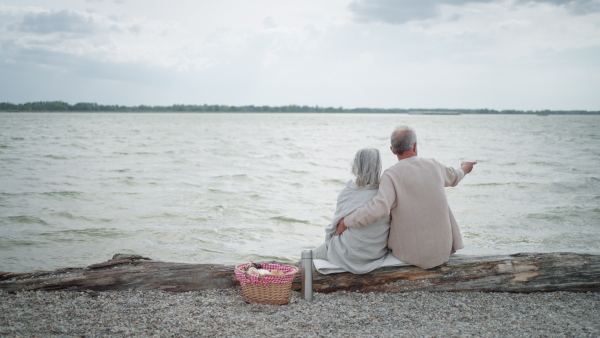 Elderly couple sitting on beach, looking at the water. Rare view. Full lenght shot.