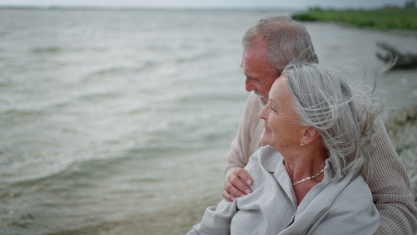 Elderly couple sitting on driftwood, embracing tenderly, enjoying time together at the beach.