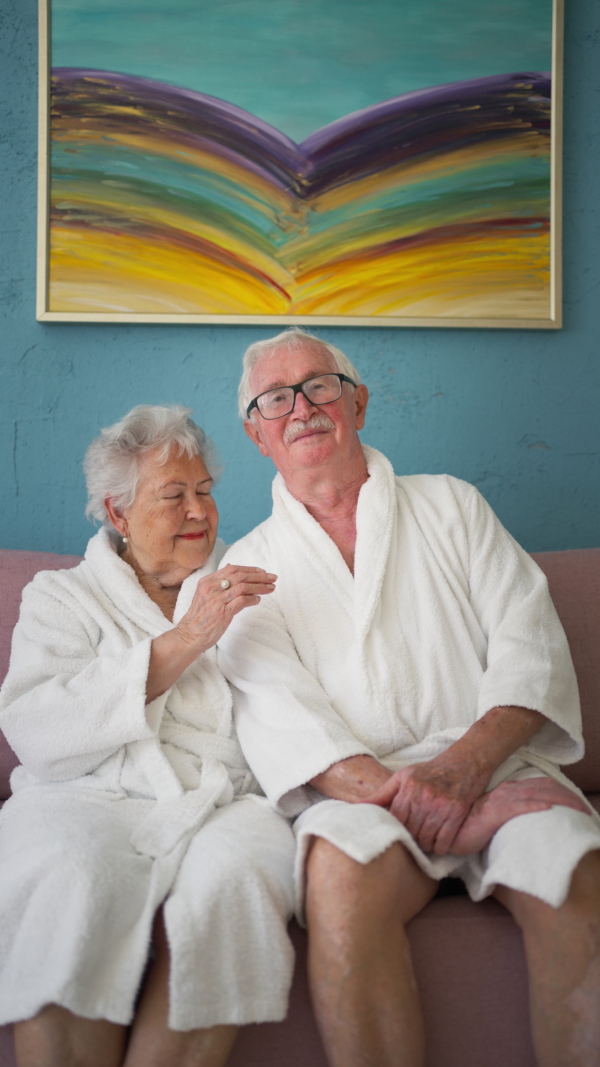 Happy senior couple sitting at a sofa in bathrobes and watching TV.