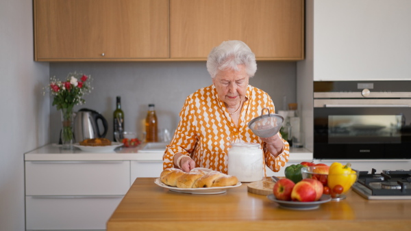 Happy senior woman sugaring a homemade sweet braided bread with raisins.