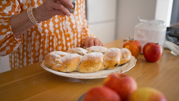 Happy senior woman sugaring a homemade sweet braided bread with raisins.