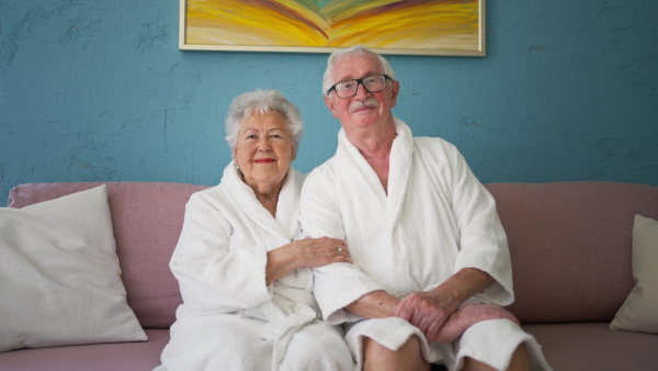 Happy senior couple sitting at a sofa in bathrobes and watching TV.