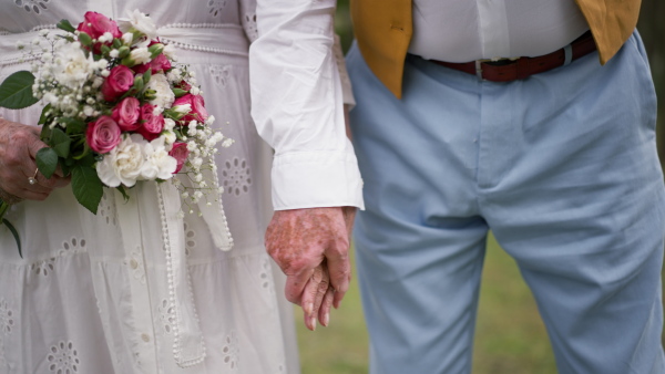 Mid section of senior hands with wedding bouquet and golden wedding rings during their marriage.