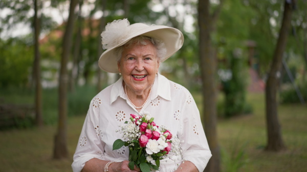 Senior woman having wedding in nature, posing with wedding bouquet.