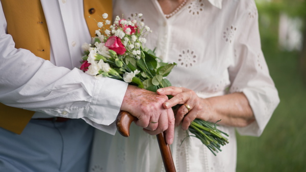 Mid section of senior hands with wedding bouquet and golden wedding rings during their marriage.