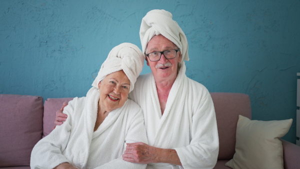 Happy senior couple sitting at a sofa in bathrobes and watching TV.