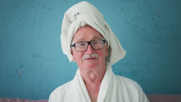 Happy senior man in glasses sitting at sofa in bathrobes and looking at camera.