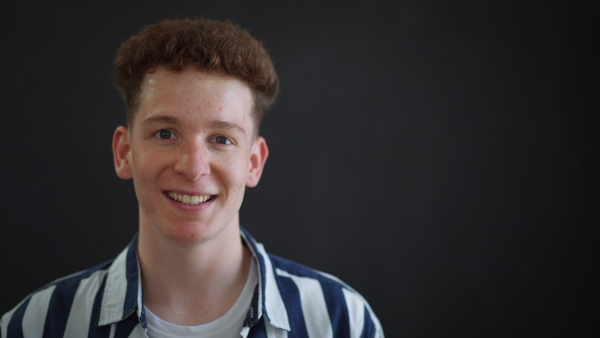 A happy young redhead man with freckles standing over dark background, copy space