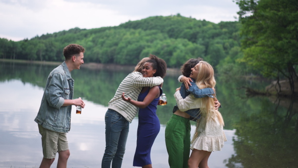 A multiracial group of young friends meeting and hugging by lake in summer.