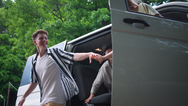 A multiracial young friends travelling together by car, getting out from the car - summer vacation, holidays, travel, road trip and people concept.