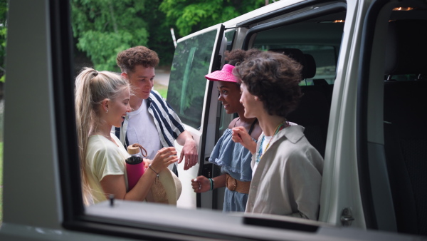 A multiracial young friends travelling together by car, standing by car and talking - summer vacation, holidays, travel, road trip and people concept.