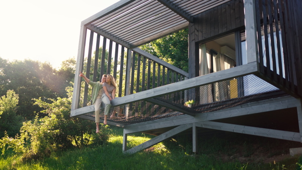 A young couple sitting and cuddling in hammock terrace in their new home in tiny house in woods, sustainable living concept.